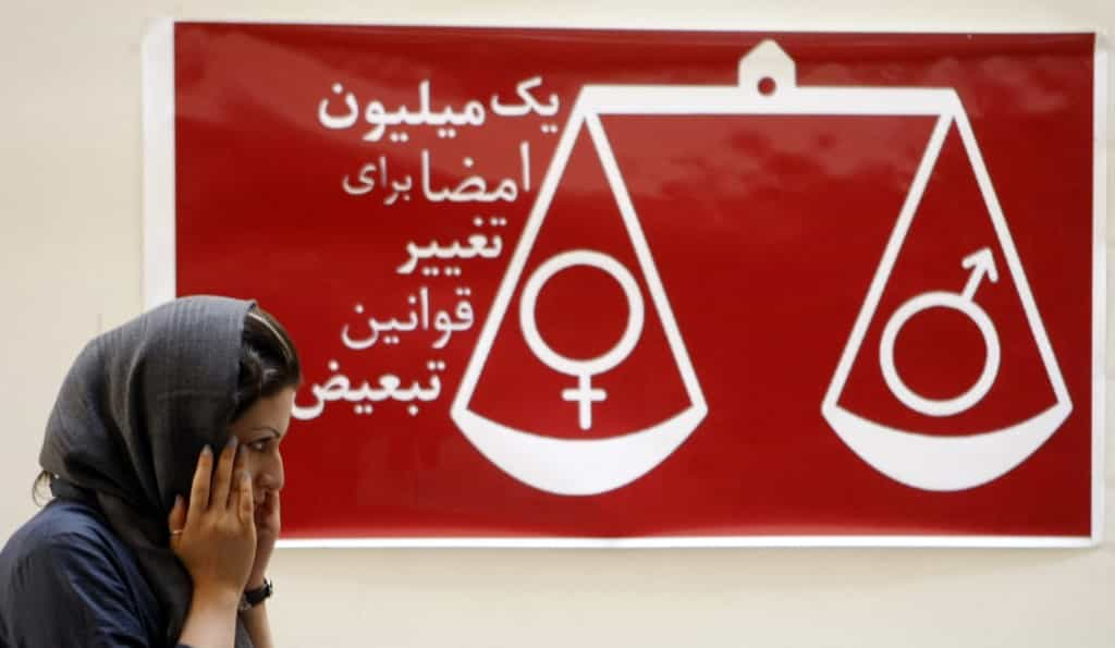 An Iranian woman walks past a banner reading "one million signatures to change the biased laws" and bearing a scale balancing female and male symbols during a press conference in Tehran, 27 August 2007. Iranians petitioning to achieve equal rights for women and men in Iran said today they hoped that their efforts would help change people's mentalities on the matter. AFP PHOTO/BEHROUZ MEHRI (Photo by Behrouz MEHRI / AFP)