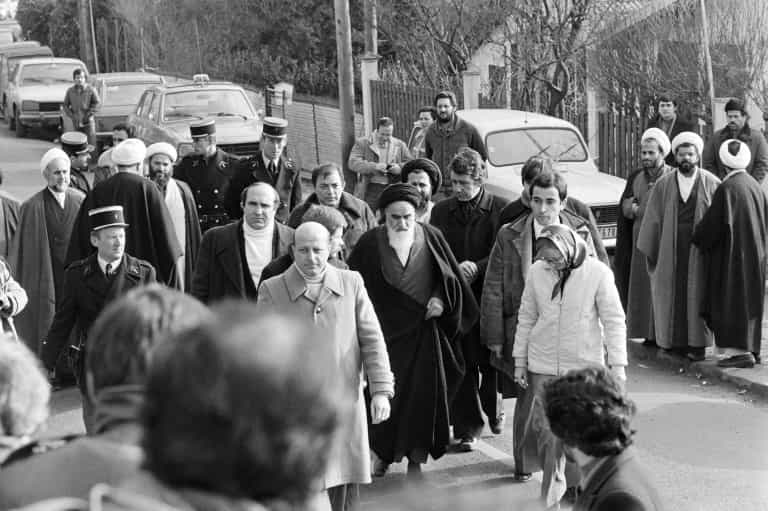 خمینی برای بازگشت به ایران نوفل لوشاتو را به سوی فرودگاه ترک میکند؛ دومین شخص در عقب تصویر با عمامه و عینک، حسن روحانی، رئیسجمهوری کنونی در میان دیگر همراهان است ــ عکس: AFP