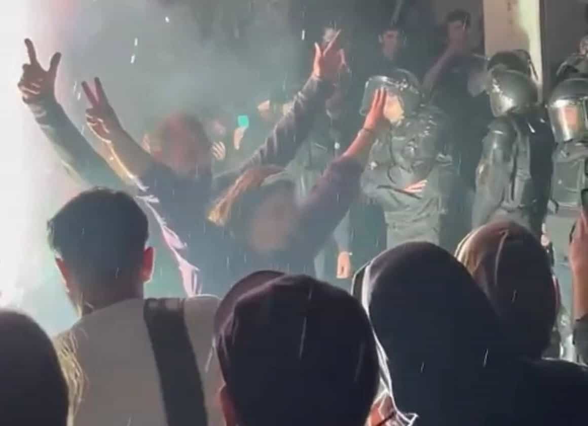 یک تصویر از شامگاه ۲۲ اسفند در خیابان: زنان و مردان در مقابل دیدهگان پلیس ضد شورش دستهایشان را به نشانه پیروزی بالا بردهاند.