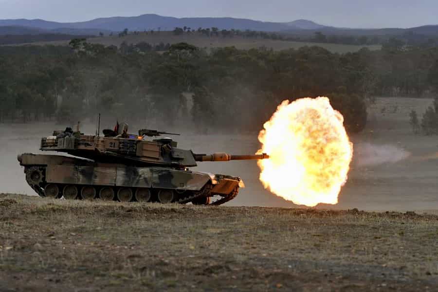 یک تانک M1A1 آبرامز ارتش استرالیا روی یک تپه در فضای جنگی شلیک کرده و از لوله آن آتش به بیرون جهیده است.