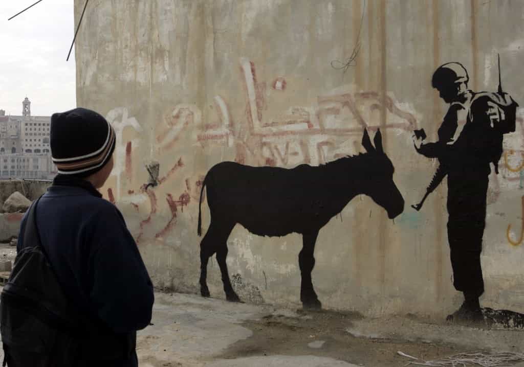 یکی از کارهای بنکسی در بیت‌اللحم در کرانه باختری. یک سرباز اسرائیلی گذرنامه یک الاغ را کنترل می‌کند. عکس: خبرگزاری فرانسه