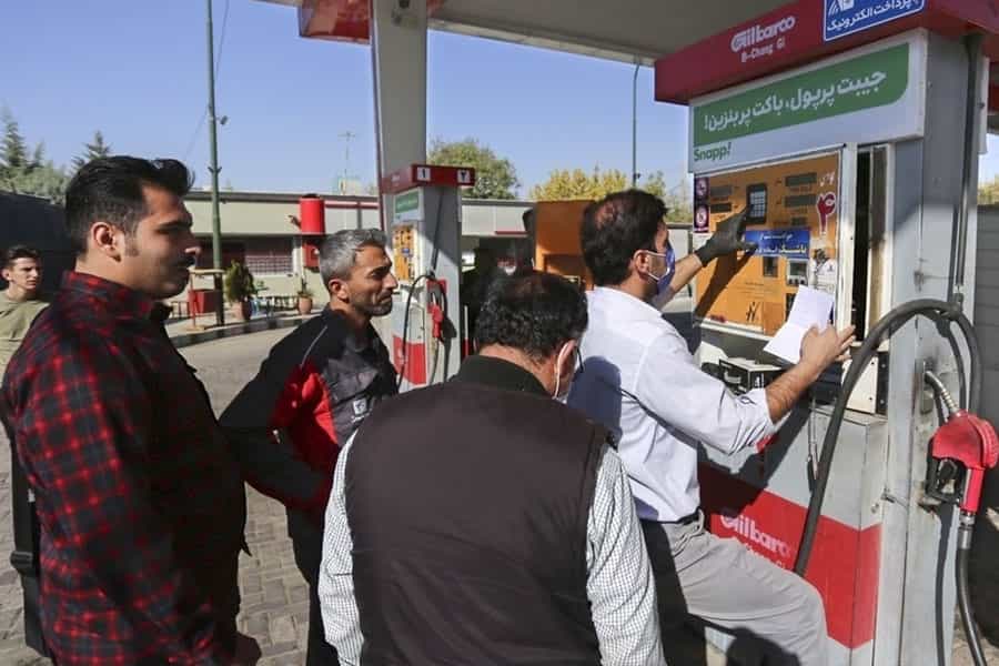 در تصویر چند مرد در جایگاه سوخت ایستادهاند و یک نفر دارد به دستگاهی که ظاهراً از کار افتاده است کُد میدهد.