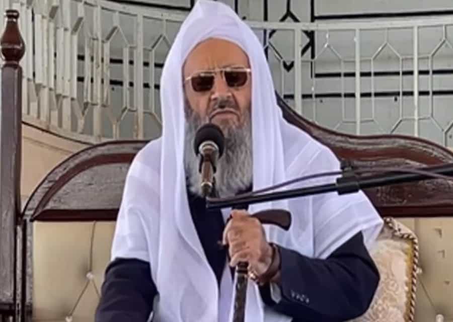 عبدالحمید اسماعیلزهی با ردای سفید و عینک آفتابی و عصا در دست پشت بلندگو