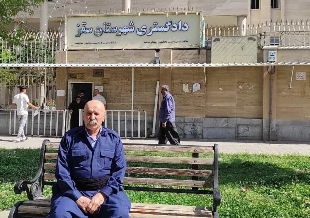 عثمان اسماعیلی، کارگر نقاش سقزی. در پشت سر او تابلو دادگستری شهرستان سقز نمایان است.
