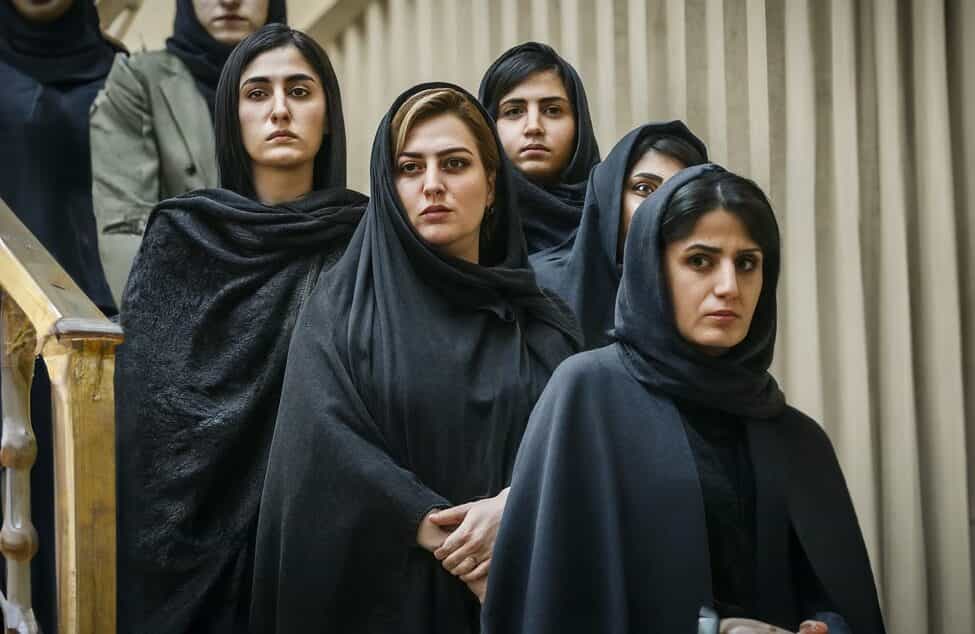 شش زن با حجاب اجباری روی پلههای یک پلکان رو به دوربین ایستادهاند.