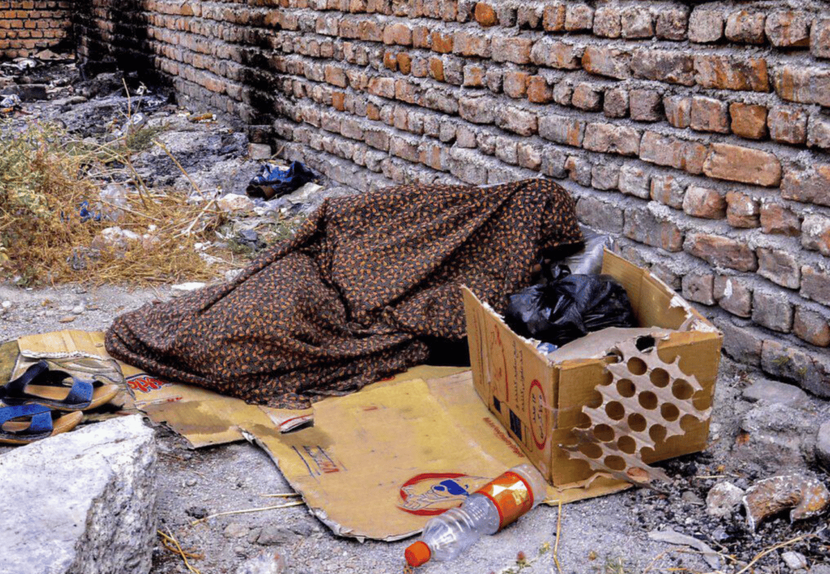 تصویری از یک زن کارتن‌خواب در تهران. او روی یک جعبه کارتنی بازشده خوابیده و چادرش را روی سرش کشیده است - تاریخ عکس نامعلوم است. عکس از راحله حصاری/ایرنا