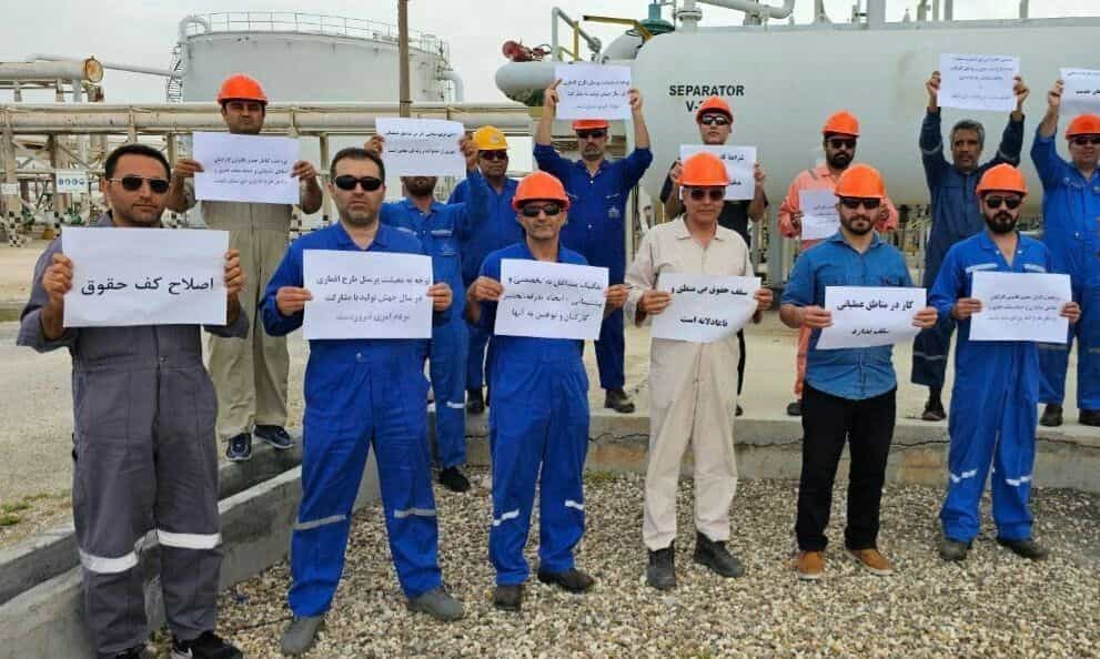 مردان کارگر رو به دوربین کاغذهایی را در دست دارند که مطالبههایشان روی آن نوشته شده است