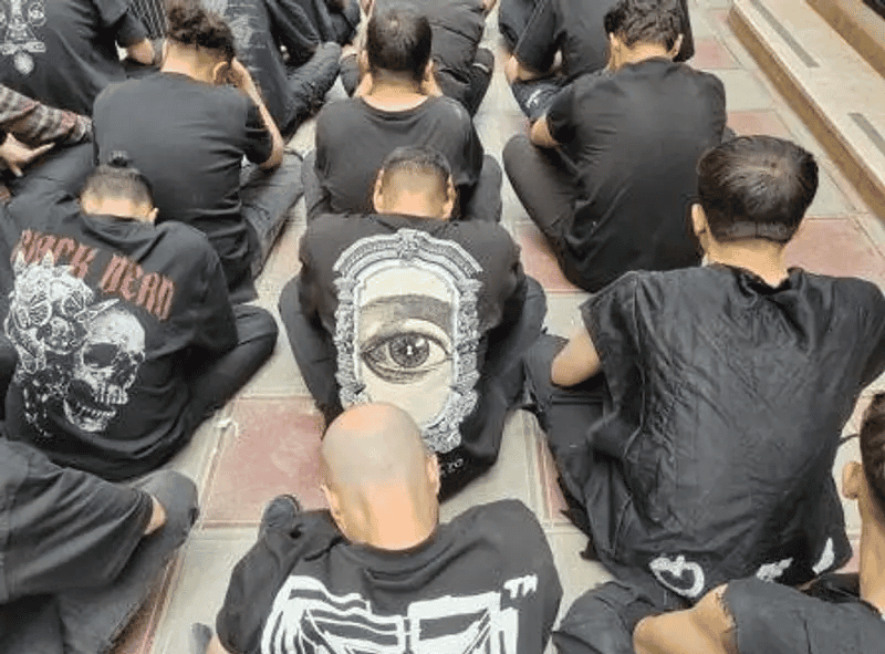 چند مرد با تیشرتهای مشکی کنار هم نشستهاند. آنها بازداشت شدهاند و دوربین از پشت سر نشانشان میدهد.
