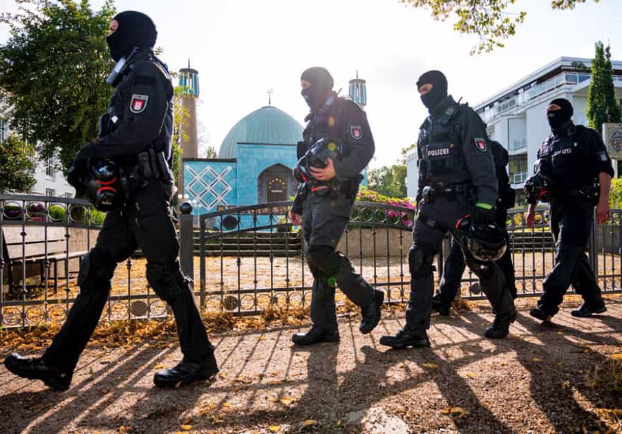 چند مأمور پلیس آلمان که چهرههای خود را پوشاندهاند از روبهروی مسجد شیعیان هامبورگ عبور میکنند.