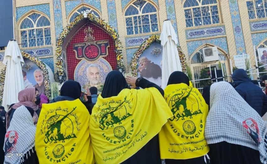 چند زن در حال دادن سلام نظامی به تصویر قاسم سلیمانی و ابومهدی المهندس با پرچمهای تیپ حسینیون