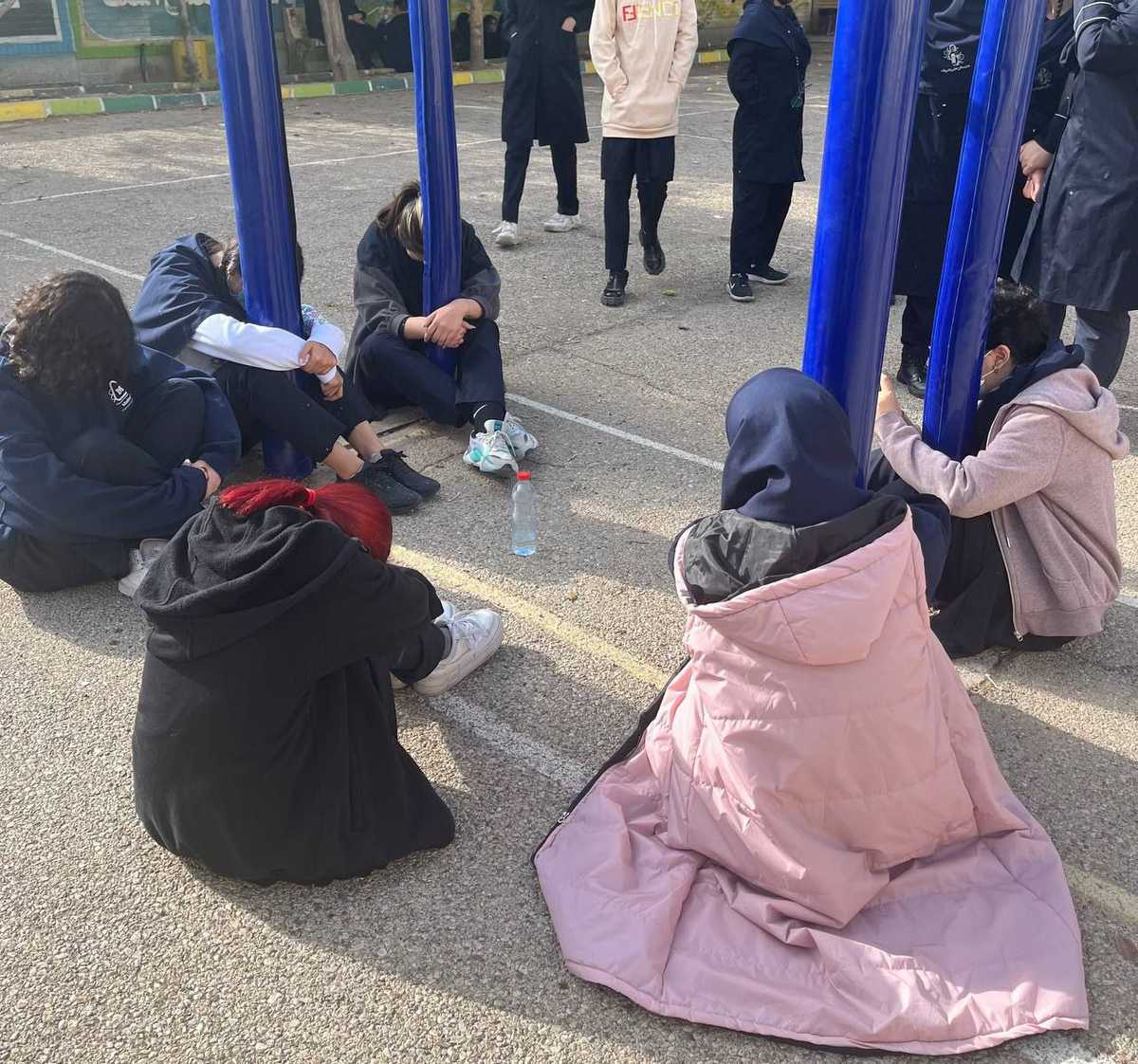پرفورمنس دانشآموزان شیرازی برای خدانور لجهای - چند دانشآموز دختر روزی زمین نشسته و صحنه بسته شدن خدانور به میله پرچم با دستان بسته را بازسازی کردهاند