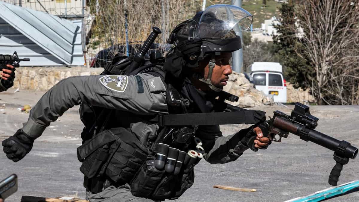 یک سرباز اسرائیلی، سلاح در دست، در حال دویدن به سمت معترضان فلسطینی است