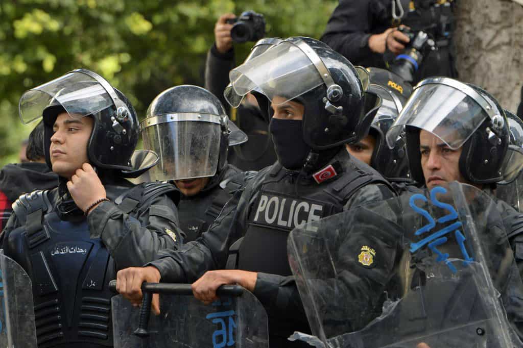 در عکس چند مأمور ضدشورش پلیس تونس با کلاهخودهای خود نشان داده میشود که در پای درختی با سپرهای خود ایستادهاند.