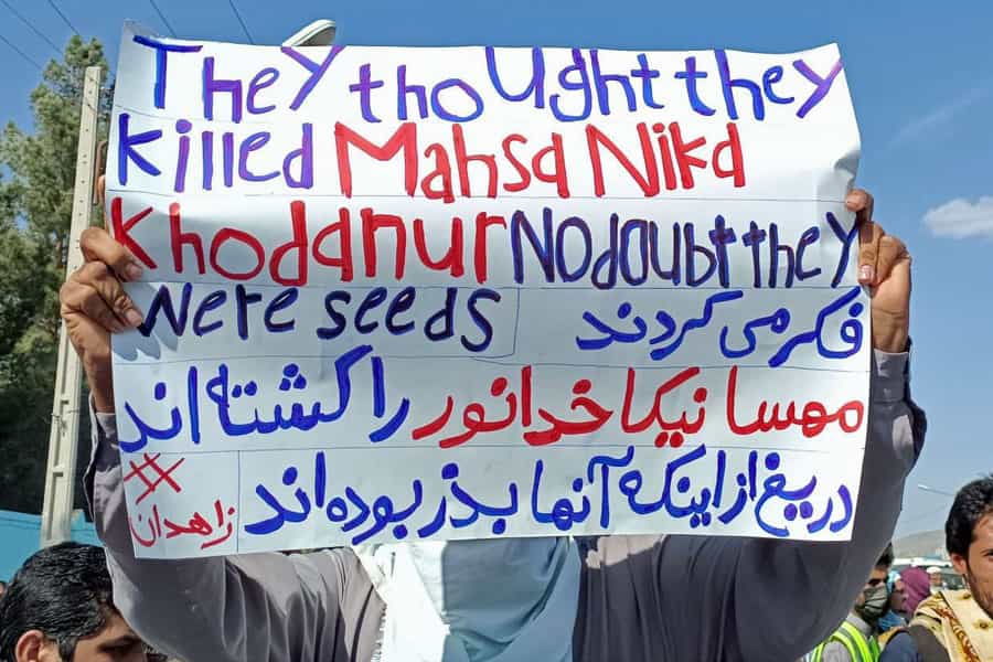 یک مرد بلوچ در اعتراضات جمعه ۵ اسفند ۱۴۰۱ زاهدان نوشتهای در دست دارد با این مضمون: فکر میکردند مهسا، نیکا و خدانور را کشتهاند دریغ از اینکه آنها بذر بودهاند