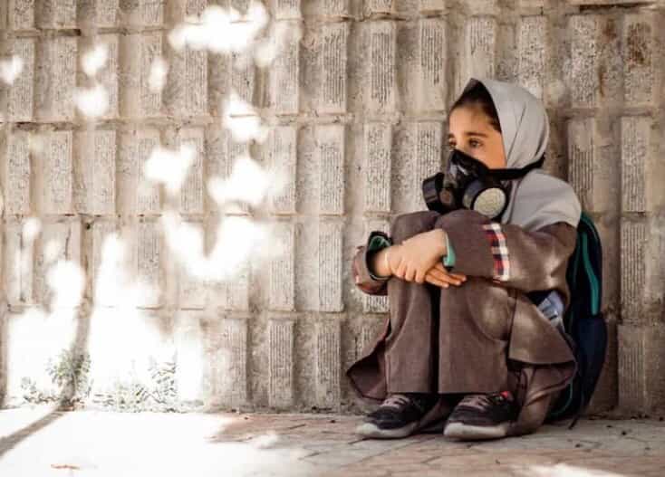 دختری دانشآموز با ماسک شیشمایی نشسته است