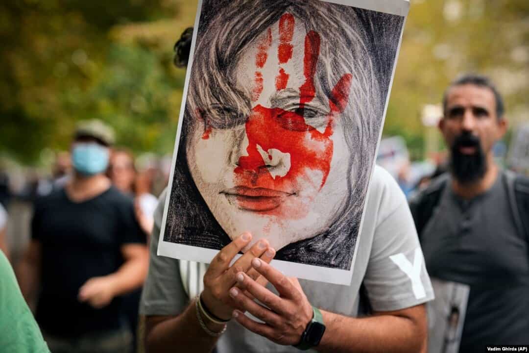 یک مرد تصویر ژینا (مهسا) امینی را در دست دارد که روی صورتش یک دست خون‌آلود کشیده شده است.