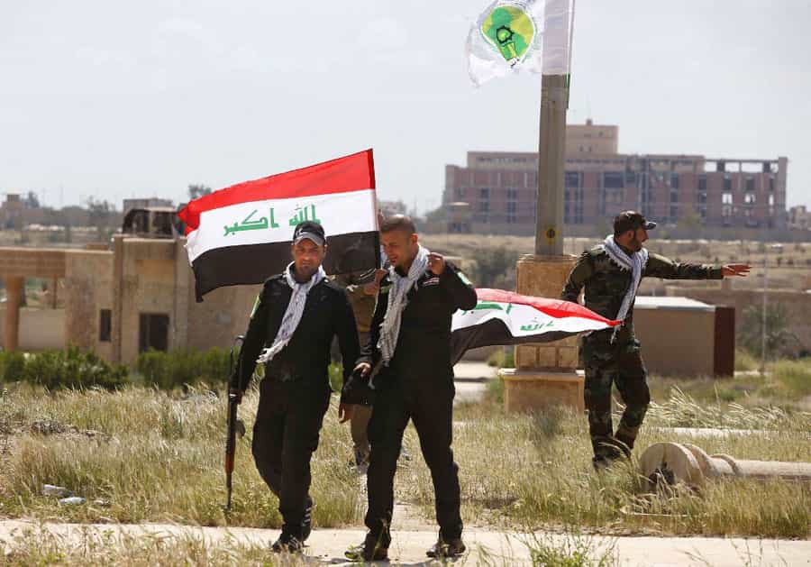 در تصویر سه نفر از شبهنظامیان حشد الشعبی عراق در کنار پرچم این کشور دیده میشوند.