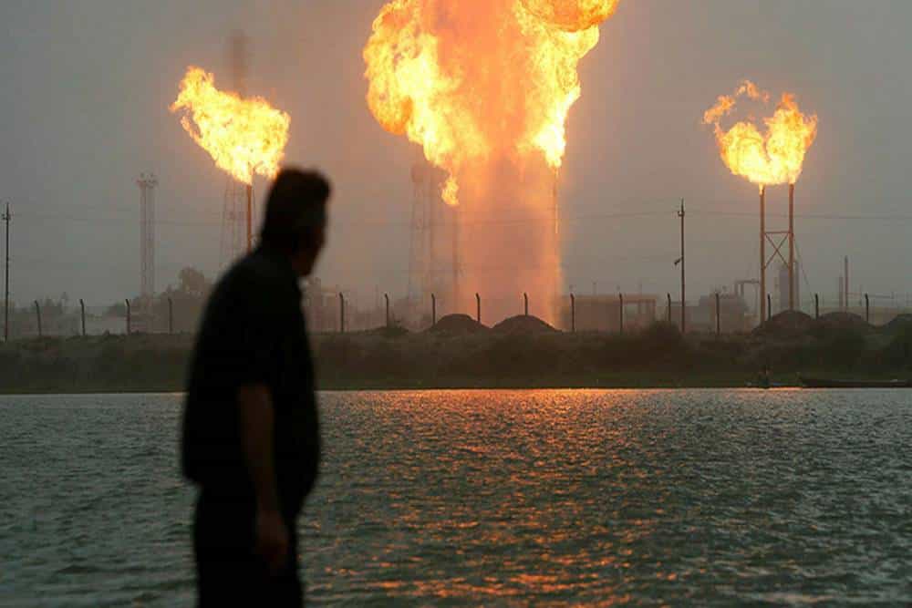 نمایی از مردی که در پس زمینه او چاه های افروخته قرار دارند.