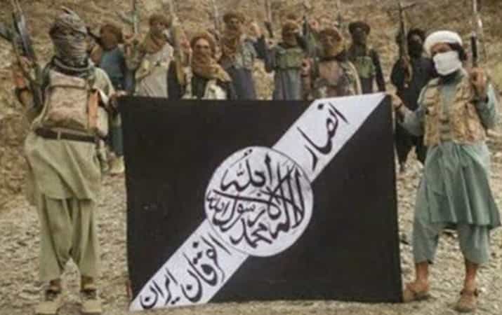 مردانی سر و صورت بسته اسلحه به دست که یک تابلو سیاه که بر روی آن نوشته شده انصار الفرقان ایران را در دست دارند.
