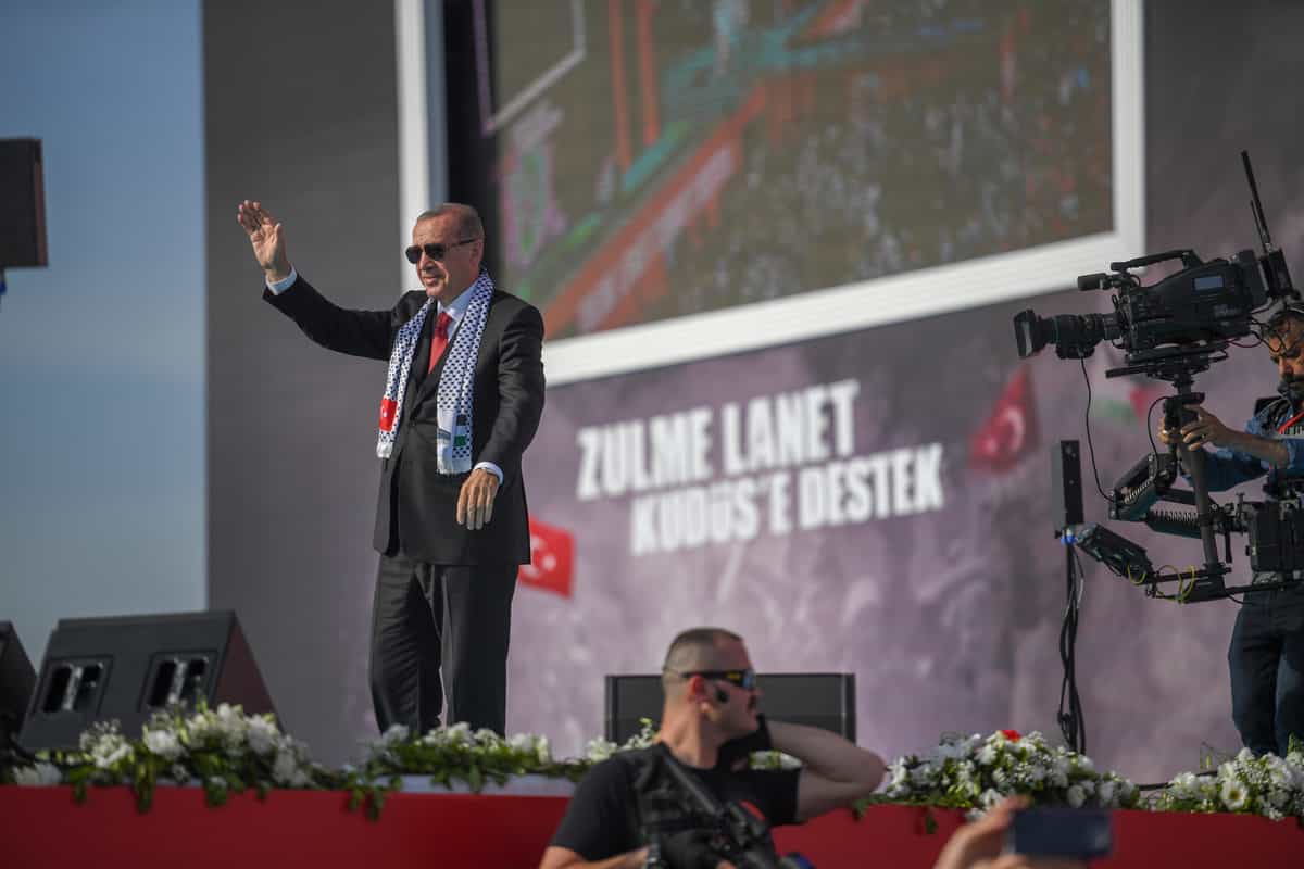 اردوغان روی یک سن ایستاده و خطاب به حاضران لبخند میزند و دست تکان میدهد