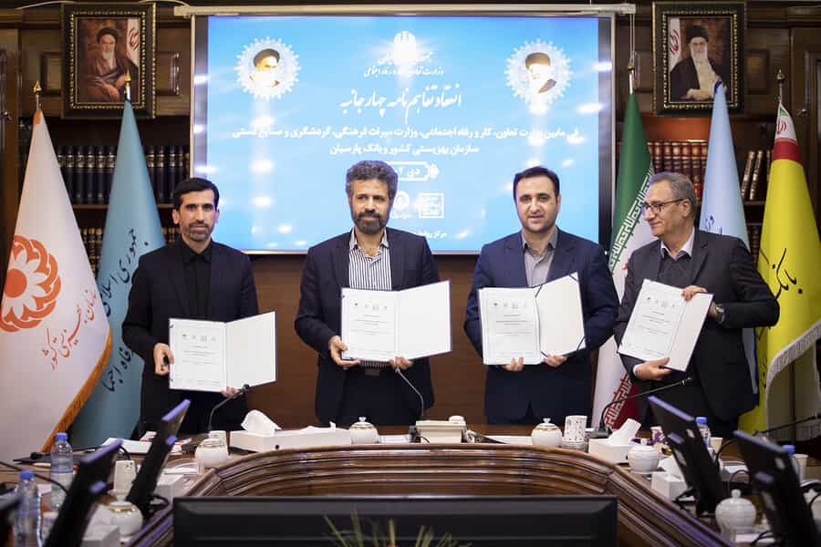 چهار مرد که هر کدام نسخهای از یک قرارداد را در دست دارند، جلوی صفحه نمایش آبیرنگی با عکس خامنهای و خمینی ایستادهاند و رو به دوربین لبخند میزنند.