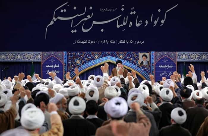 دیدار امامان جمعه با علی خامنهای. در بالای سر او به فارسی و عربی نوشته شده مردم را نه با گفتار بلکه با کردار دعوت کنید.