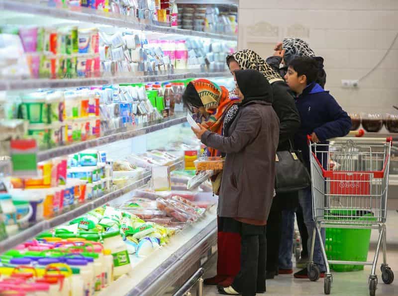 چند زن و یک کودک با سبد خرید خالی در کنار قفسه گوشت و لبنیات به قیمتها نگاه میکنند.