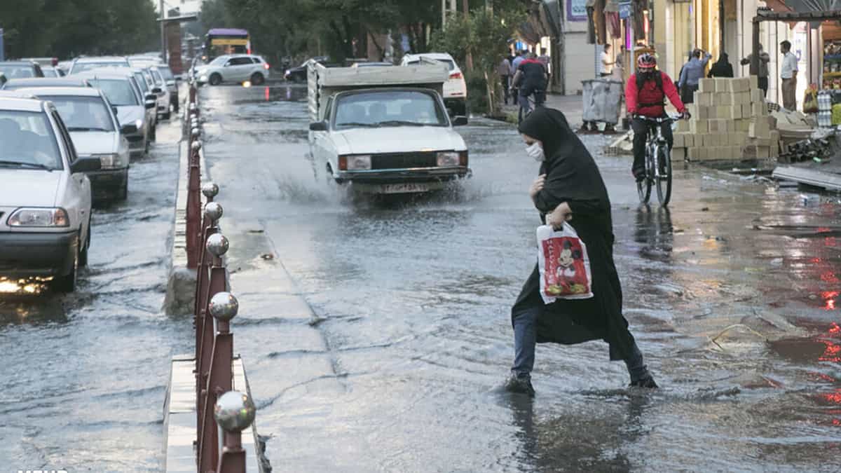 یک خیابان آبگرفته. ماشینها و عابران باوجود آبگرفتگی در خیابان میروند