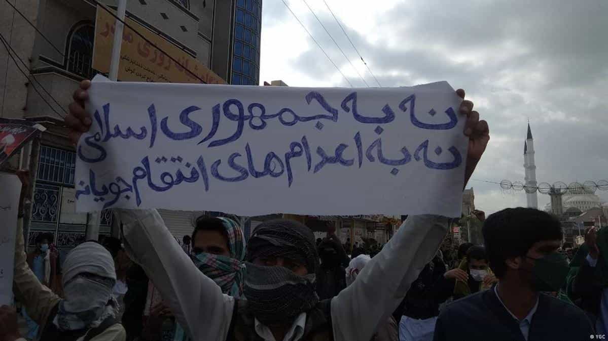تصویری از یک تجمع اعتراضی در زاهدان. یکی از تظاهرکنندگان پلاکاردی را در دست دارد که روی آن نوشته شده:«نه به جمهوری اسلامی، نه به اعدامهای انتقامجویانه»