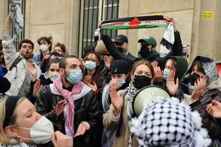 گروهی از دانشجویان که برخی از آنها ماسک پزشکی (متعلق به دوران کرونا) بر چهره دارند پرچم فلسطین را بالا بردهاند و دست میزنند.