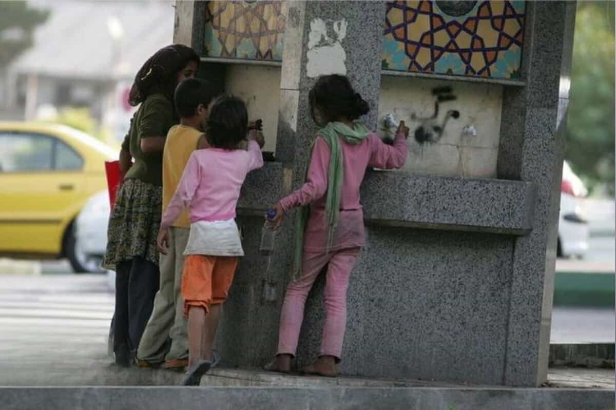 چهار کودک با لباسهای مندرس از یک آبخوری در خیابان آب میخورند