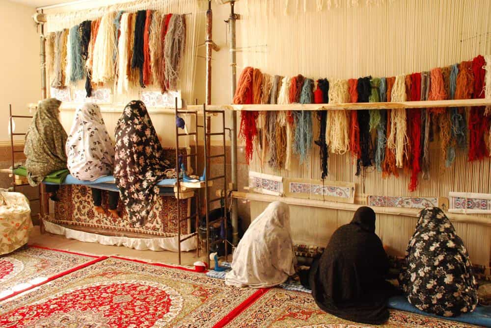 تعدادی زن پشت به دوربین رو به دارهای قالی فرش میبافند