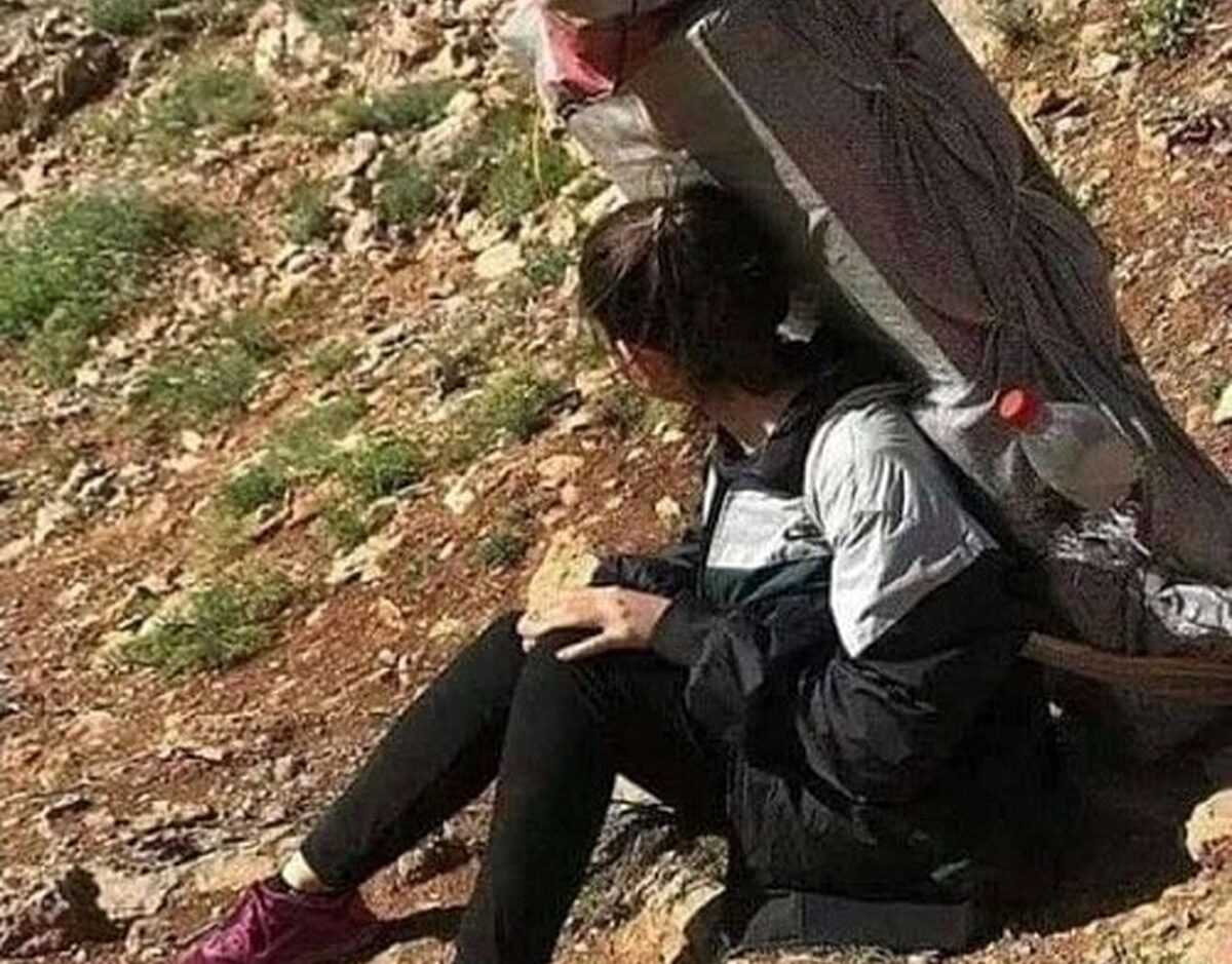 یک زن جوان کولبر بدون روسری روی یک تخته سنگ نشسته است