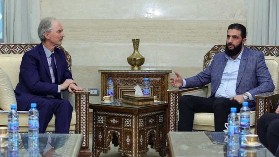 ابومحمد الجولانی با کُت خاکستریرنگ، بدون کراوات و با ریشی انبوه در حال سخنگفتن است و گیر پدرسن با دقت به او گوش میدهد.