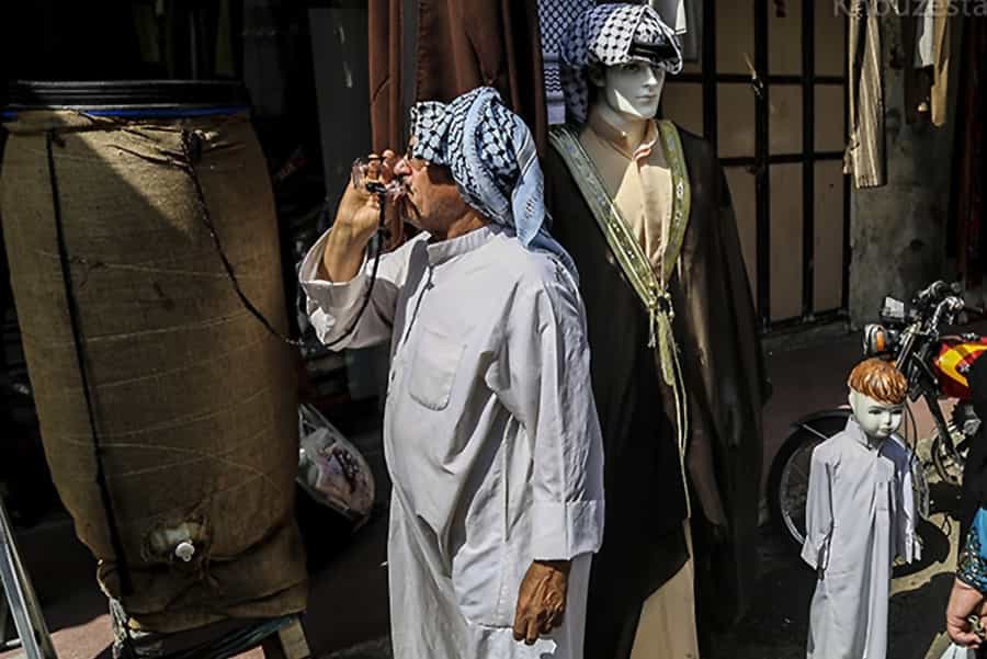 مردی با لباس عربی در اهواز در حال نوشیدن آب در خیابان