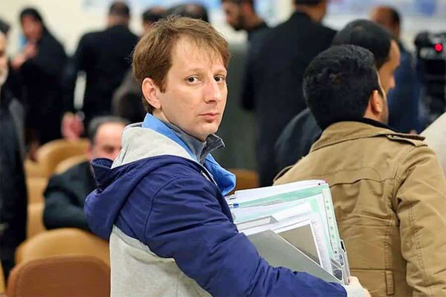 بابک زنجانی با پوشه‌هایی در دست به دوربین نگاه می‌کند.
