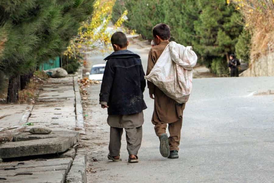 دو کودک کار افغان با کیسه‌ای بر پشت در یک خیابان دیده می‌شوند.