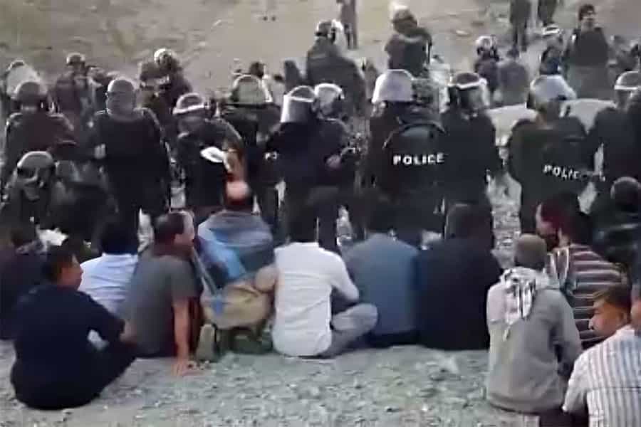 مأموران ویژه امنیتی با کلاه‌خود و باتوم چند تن از اهالی روستای دهکهان را که روی زمین نشسته‌اند، احاطه کرده‌اند.