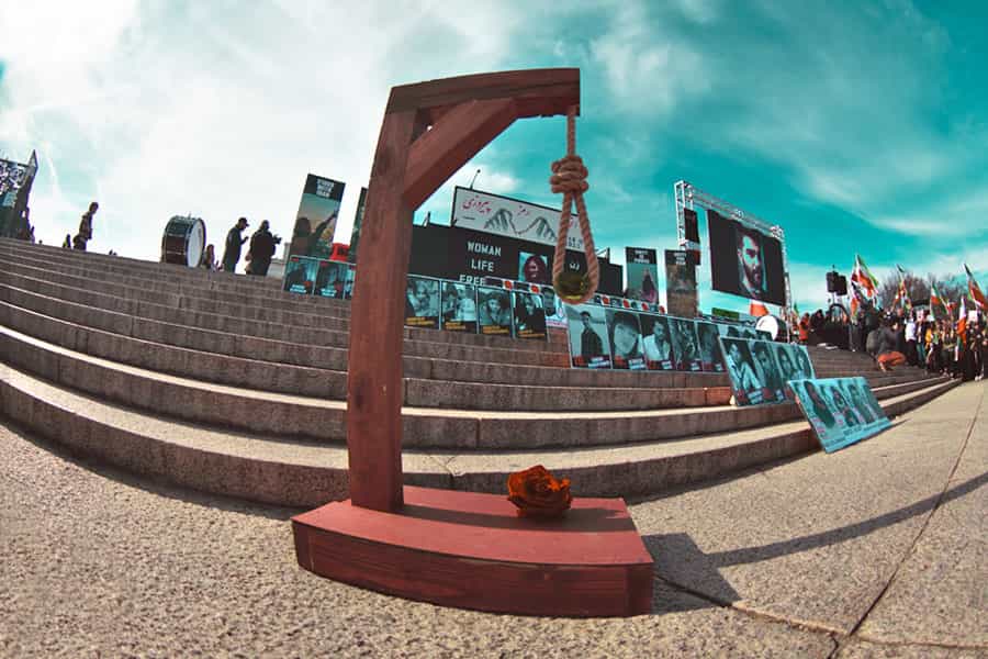 در پای پله‌هایی که جمعیت در اطراف آن گرد آمده‌اند، چوبه‌ی اعدامی به شکل نمادین بر پا شده و گل سرخی بر سکوی آن قرار دارد. روی پله‌ها تصاویری از کشته‌شدگان و اعدام‌شدگان دیده می‌شود.