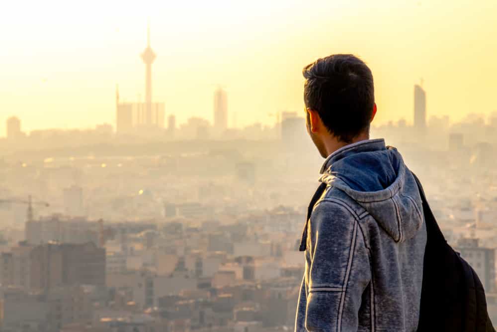 مرد جوانی پشت به دوربین و رو به نماد برج میلاد تهران به غروب نگاه میکند