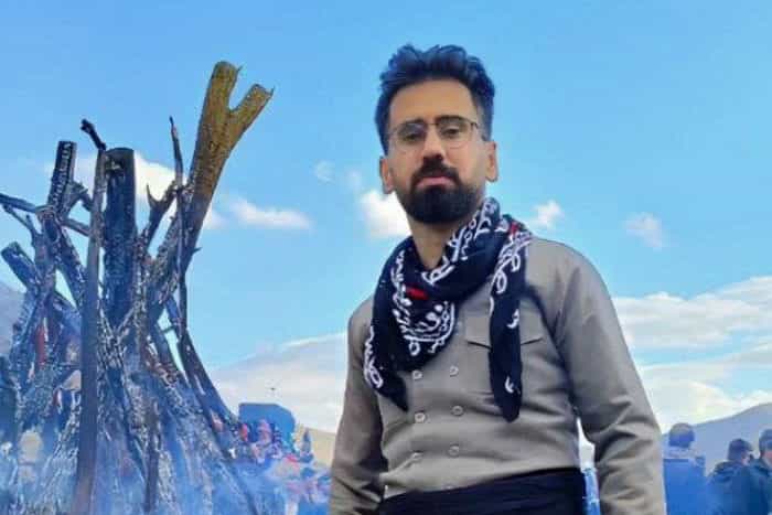 تصویری از حمید مرادی با لباس کُردی در کنار هیزمی از آتش.