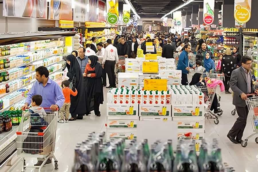 نمایی از یک فروشگاه زنجیره‌ای در ایران که خانواده‌ها با در دست داشتن سبدهای چرخدار خرید در حال تماشای اجناس هستند.