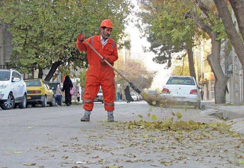 یک رفتگر (پاکبان) در خیابانهای تهران مشغول جارو زدن برگهای درختان است.