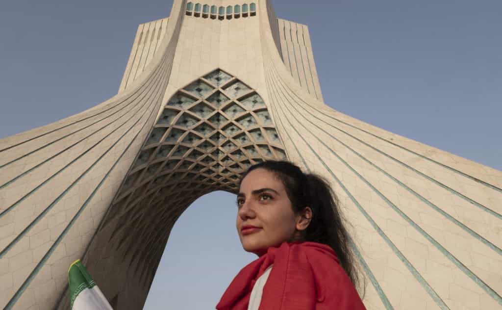 یک زن جوان ایرانی در حالی که در یک کنسرت زنده در غرب تهران، ایران، در ۲۵ ژوئن ۲۰۲۵، همزمان با آتش‌بس بین ایران و اسرائیل، در مقابل بنای یادبود آزادی ایستاده است.