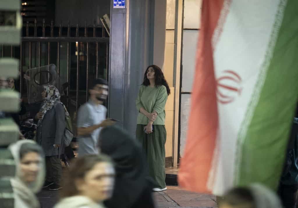 یک زن جوان ایرانی که حجاب اجباری ندارد، در یک راهپیمایی مذهبی به مناسبت سالروز تولد پیامبر محمد در مرکز شهر تهران، ایران، در 10 سپتامبر 2025، در کنار پرچم کشور ایستاده است.