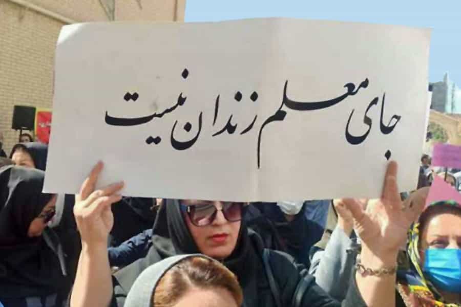 یک معلم زن در میان تجمع گروهی از معلمان زن نوشتهای با این مضمون در دست گرفتهاند: «جای معلم زندان نیست».