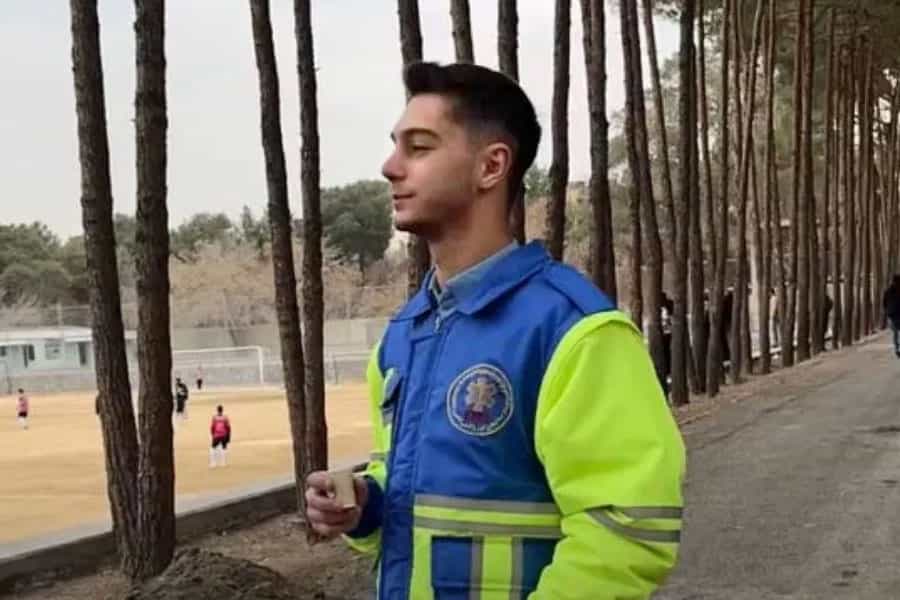 در تصویر هومن کیانی در لباس امدادگران پزشکی در کنار یک زمین فوتبال دیده میشود.