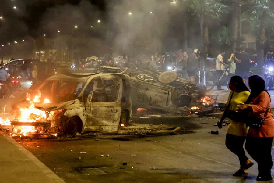 در تظاهرات جوانان مراکشی در شهر سِلا دو زن از کنار خودروهای پلیس که به آتش کشیده شدهاند، عبور میکنند.