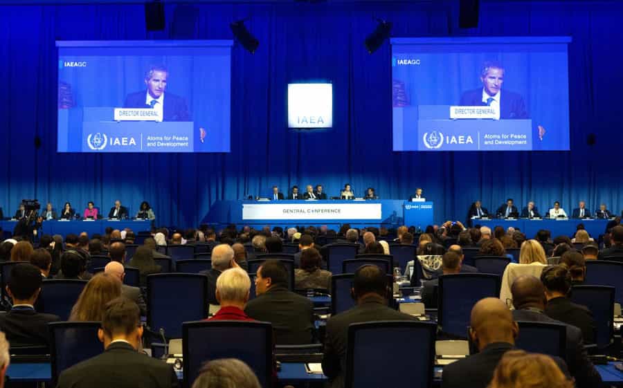 نمایی عمومی از سالن نشست آژانس بینالمللی انرژی اتمی در وین. دو مونیتور تصویر رافائل گروسی، مدیرکل آژانس را در حال سخنرانی نشان میدهند. از دور تریبون دیده میشود.