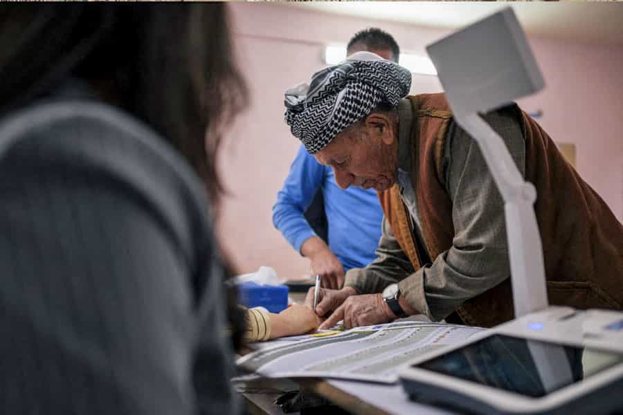 مردی با لباس کردی بر سر صندوق رأی انتخابات پارلمانی عراق در حال نوشتن است.